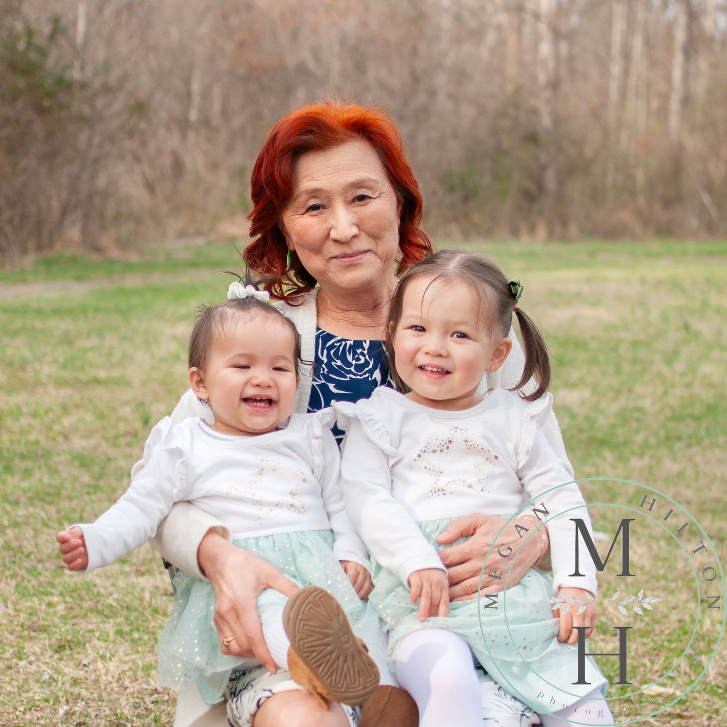 A joyful grandma with her two granddaughters together outdoors on a sunny spring day with trees and grass in the background.