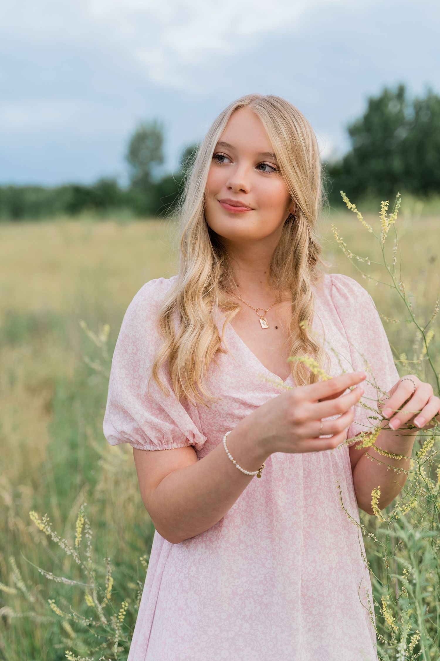 Senior student in light pink dress standing in a summer meadow with tall grass and wildflowers in Middlegrounds Metropark