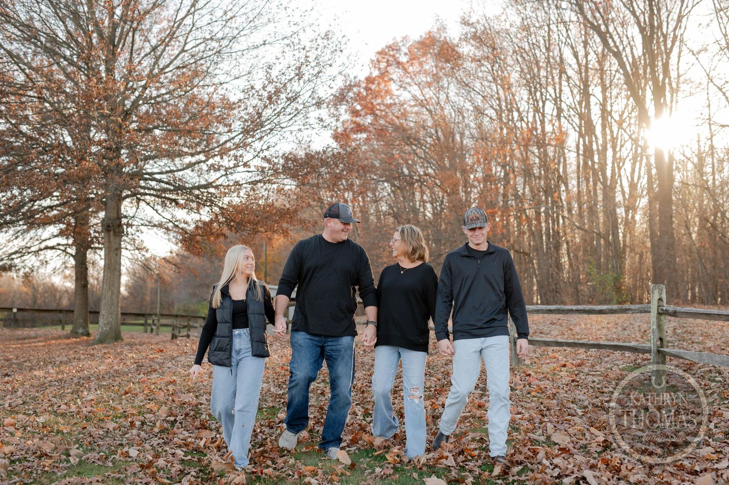 Group walking together in casual clothing through autumn landscape with wooden fence.