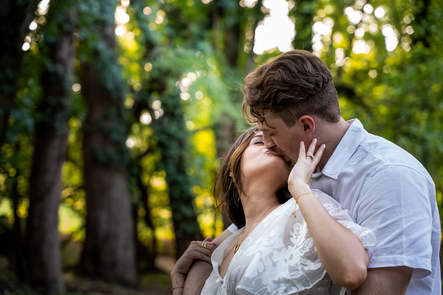 Couple embracing passionately in a sunlit forest setting.