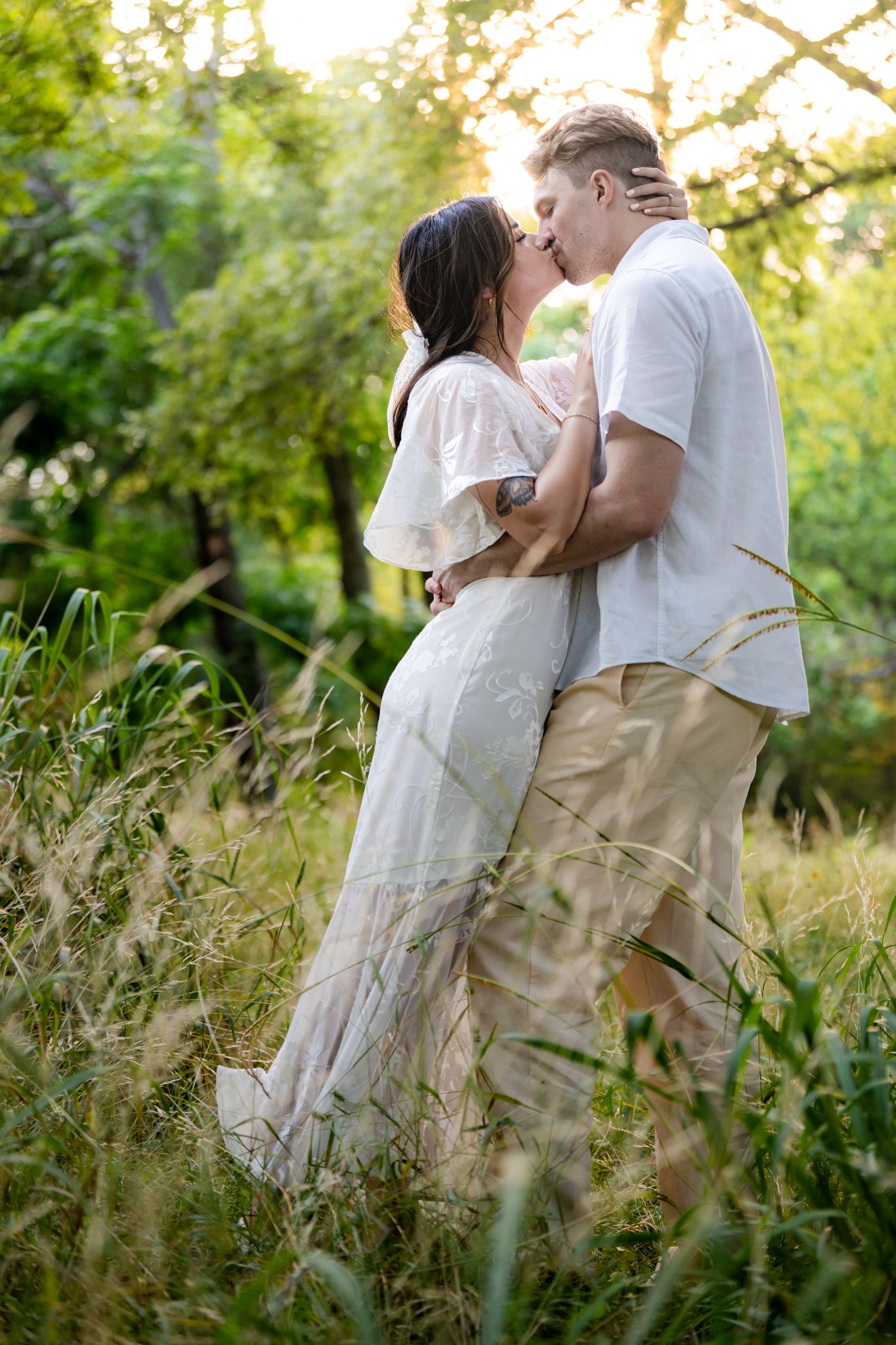 Romantic couple kissing in a field of tall grass during golden hour.
