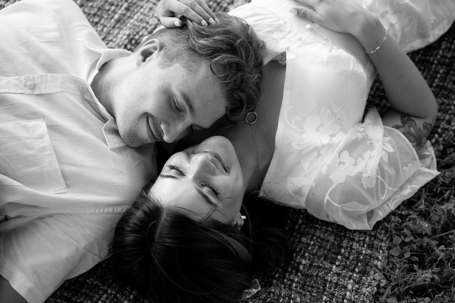 A couple lies together on a blanket outdoors in a tender black and white photograph.