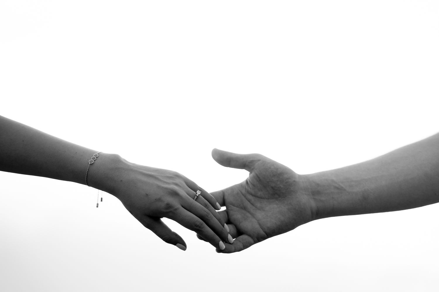 Two hands reach towards each other in a tender moment captured in black and white against a white background.