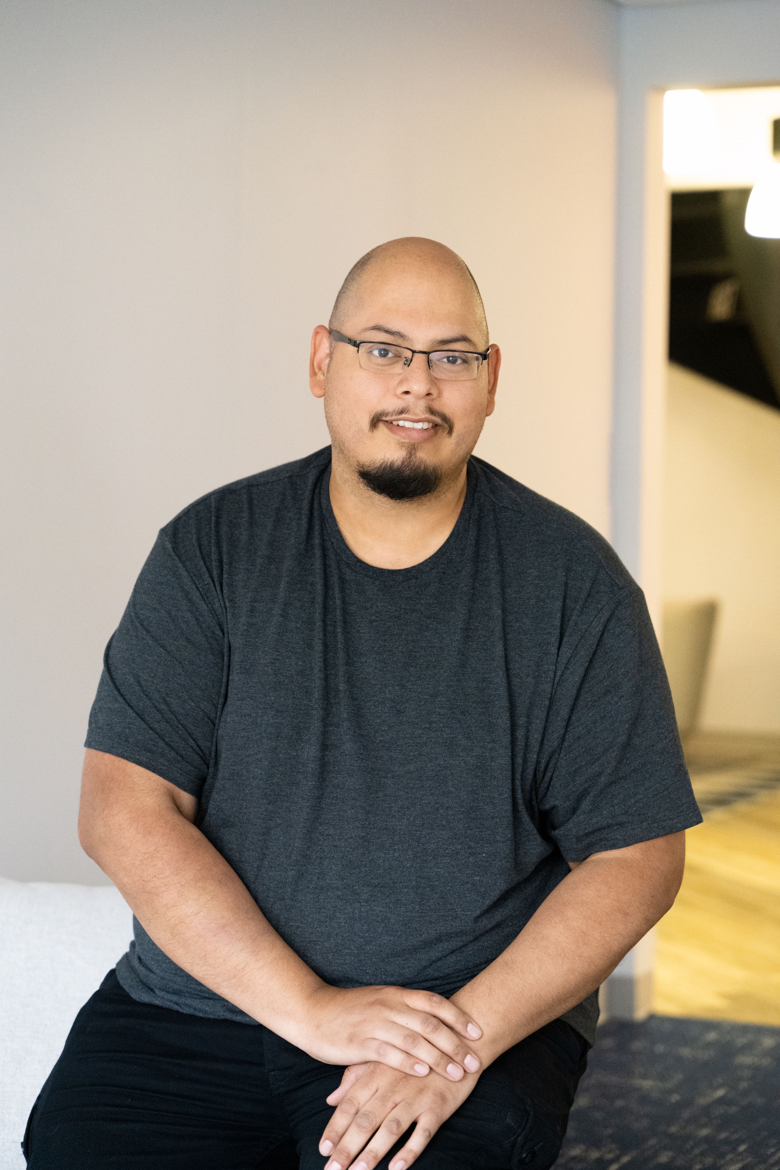 Professional headshot of Asian man in grey t-shirt against light background.