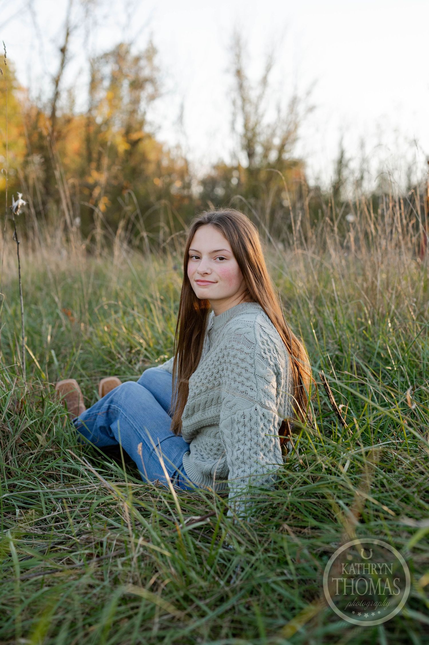 Someone in casual attire reclines in a sunlit autumn field wearing denim and a knit sweater.