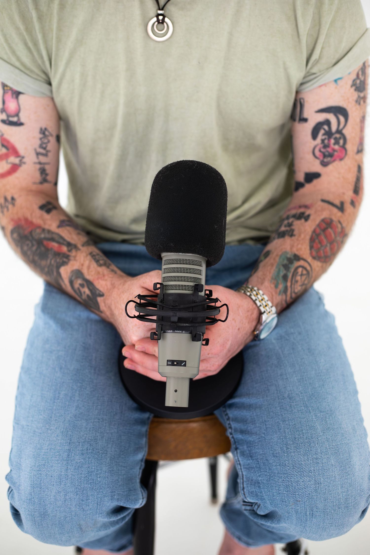 Close-up of tattooed hands holding black microphone against light background.