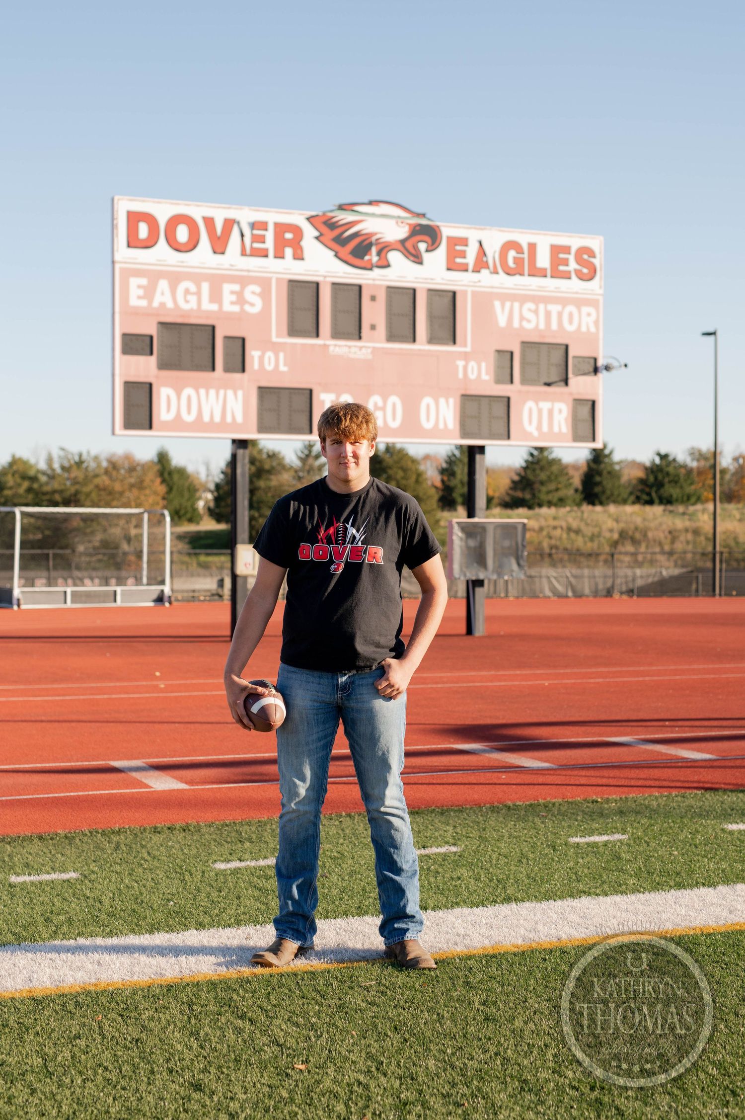 Player stands with football on field in front of Dover Eagles scoreboard during sunset.