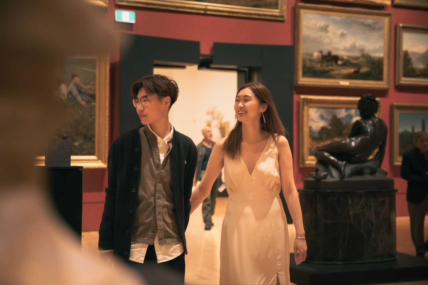 A couple walks through an elegant art museum gallery space wearing formal attire.