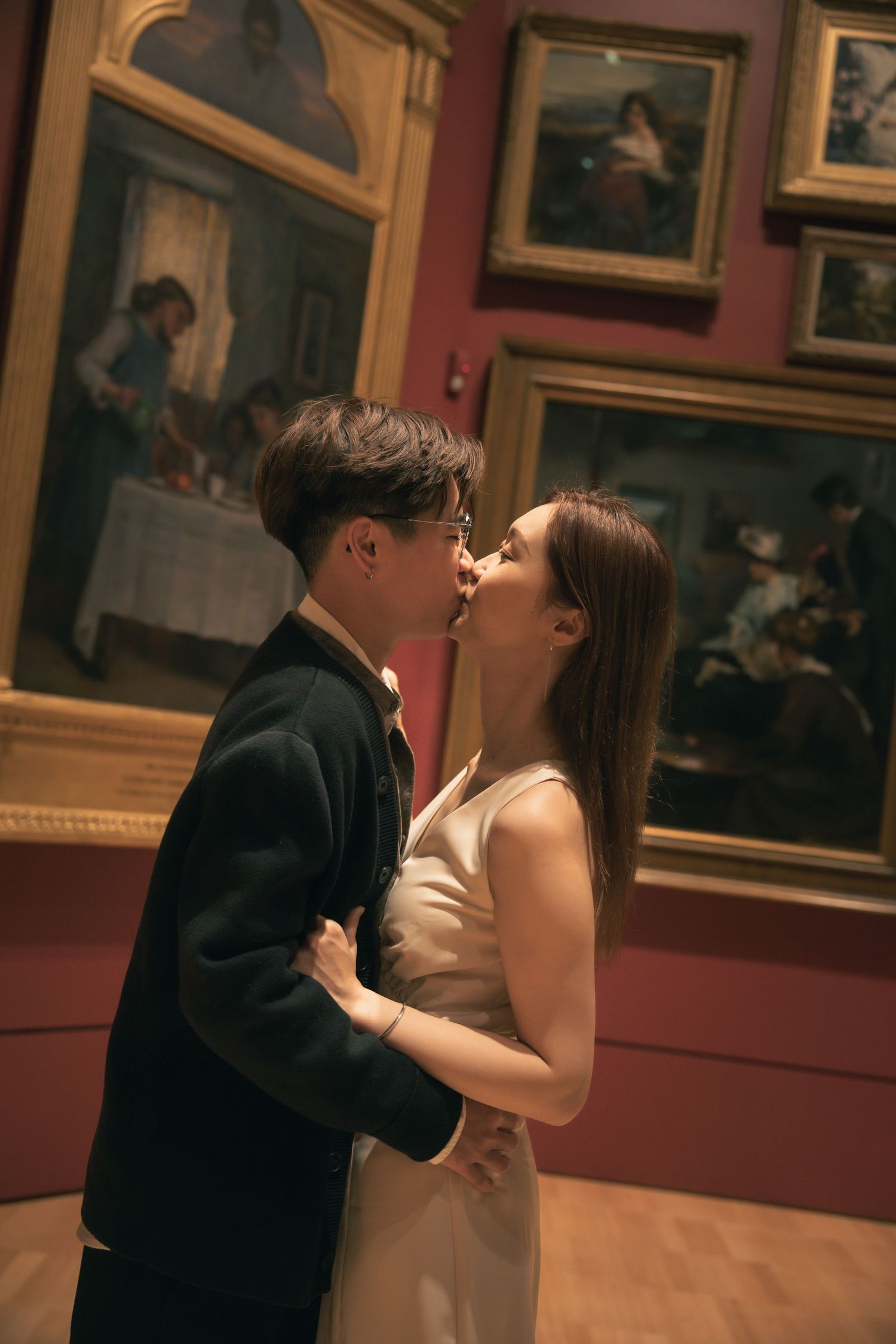 A romantic embrace captured in a museum gallery surrounded by classical artwork and gilded frames.