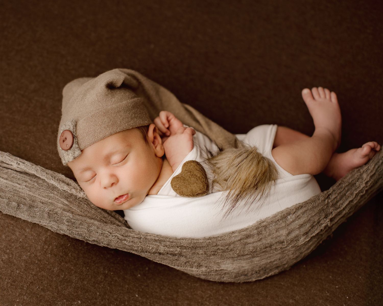 A sleeping newborn baby photographed in a rustic wooden bowl against a dark brown background. Palmerston North New Zealand