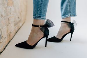 Close-up of black ankle strap stiletto heels worn with blue jeans.