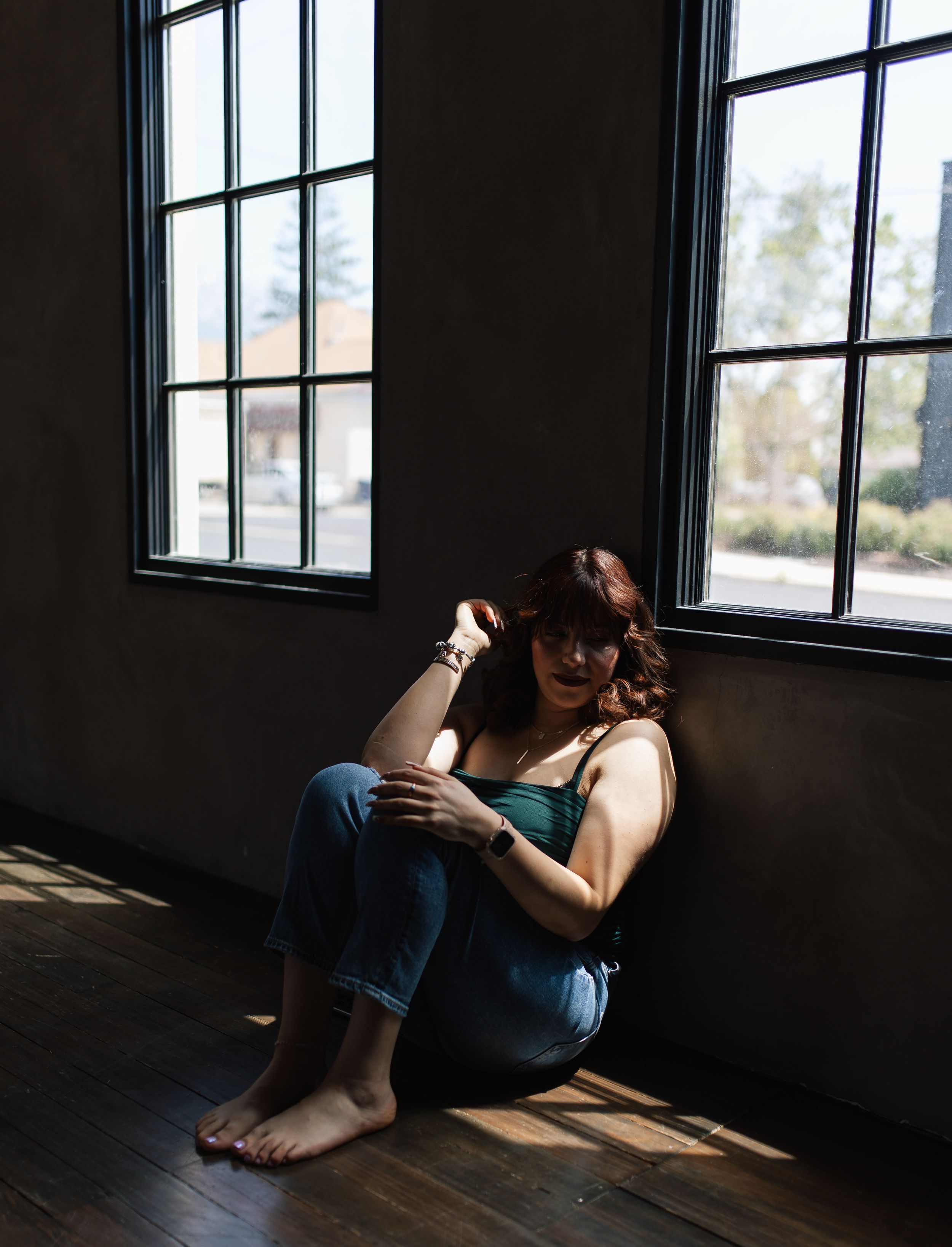 Person reading near window in casual attire while sitting on hardwood floor.