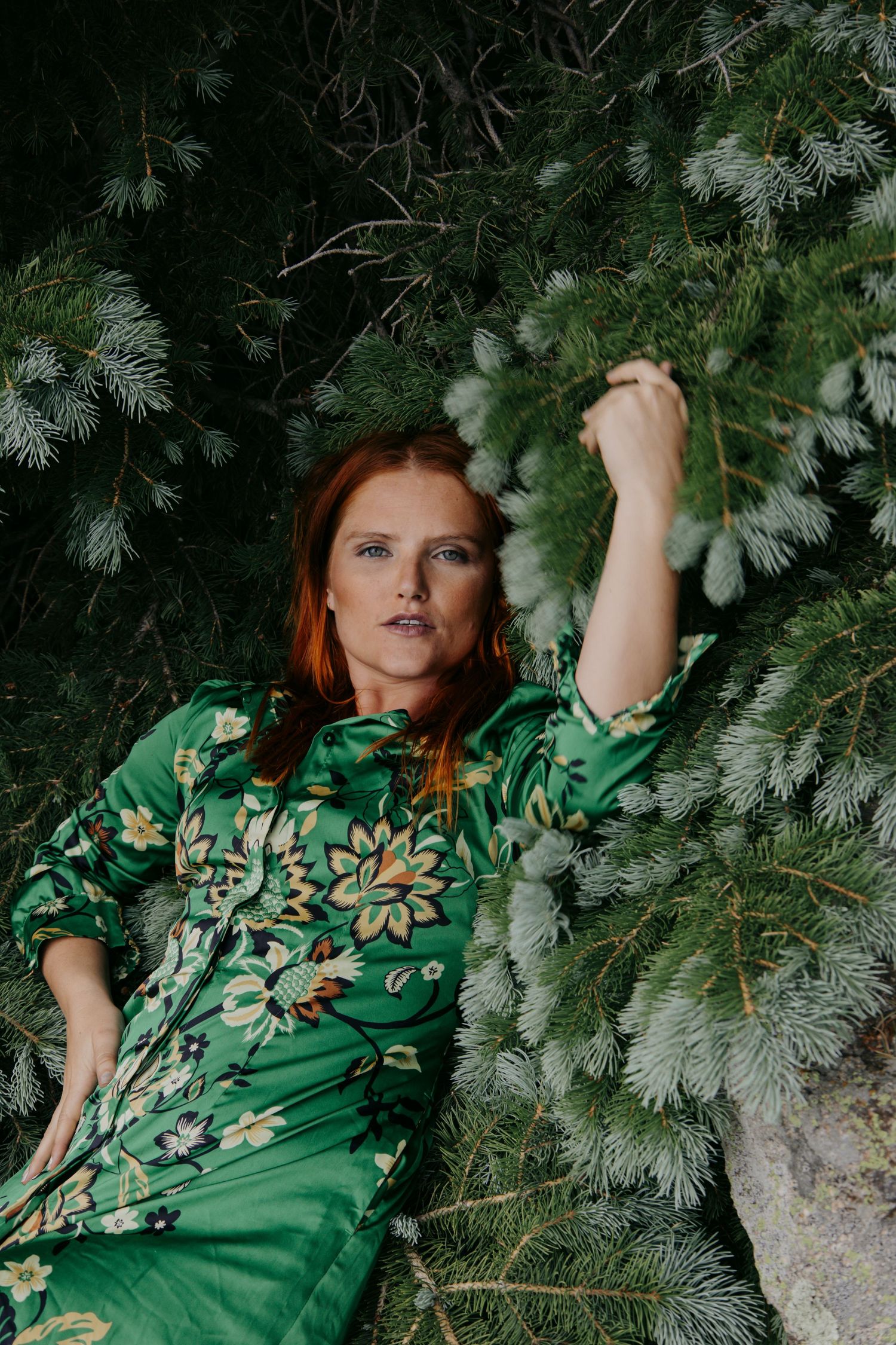 Under gnarled tree roots on a rocky beach shoreline, with a woman standing in a tropical forest backdrop.