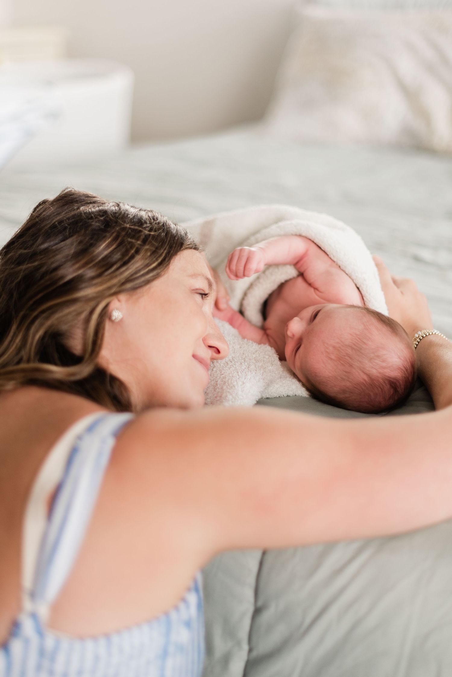 Tender moment between parent and newborn baby lying together on white bedding.
