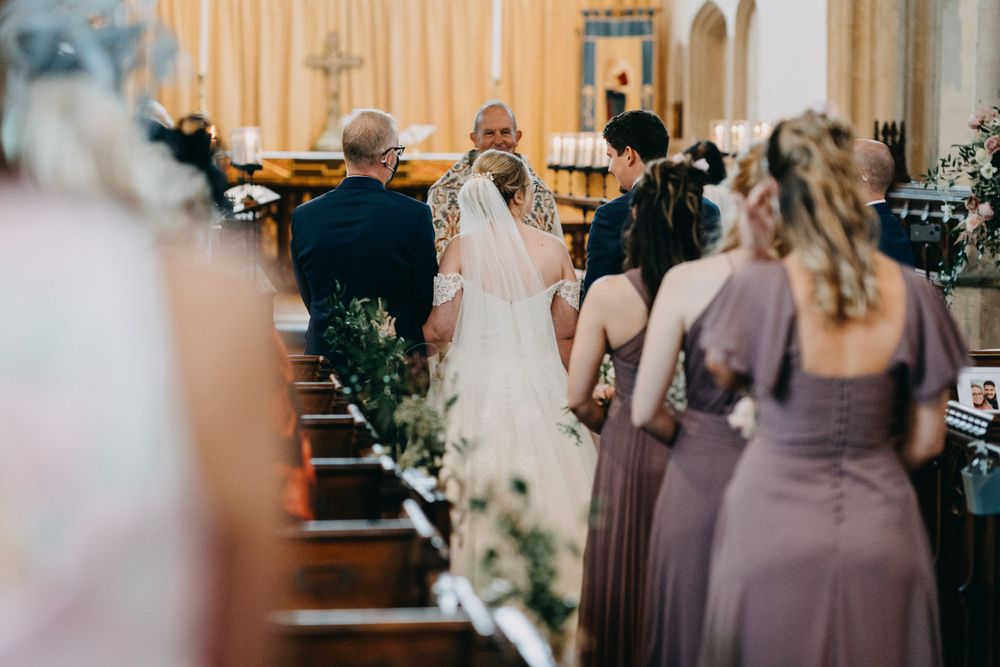 Wedding ceremony taking place inside a traditional church with purple-clad bridesmaids lining the aisle.