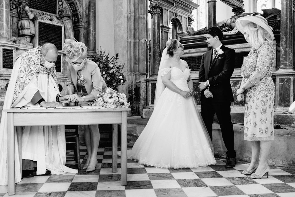 Black and white photograph of a wedding ceremony with people signing documents inside an ornate church setting.