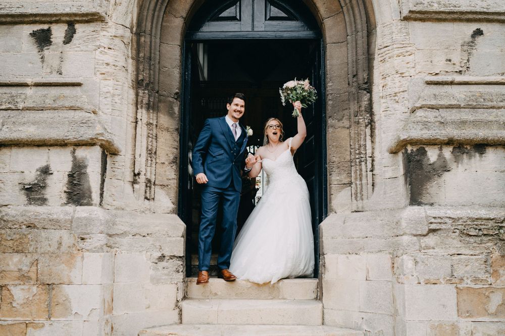 A bride and groom stand together in a historic stone church doorway during their wedding celebration.