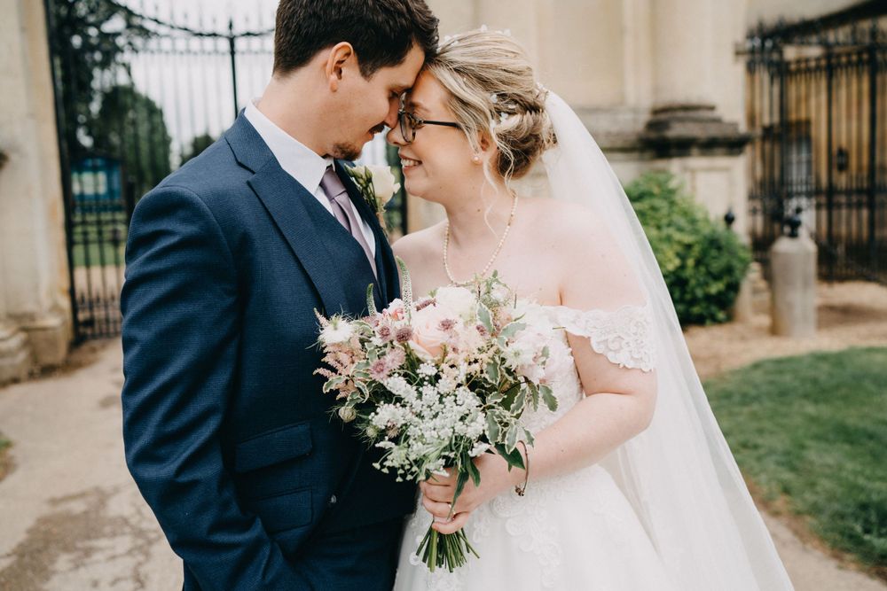 A romantic wedding couple embraces outdoors while holding a soft pink and white floral bouquet.