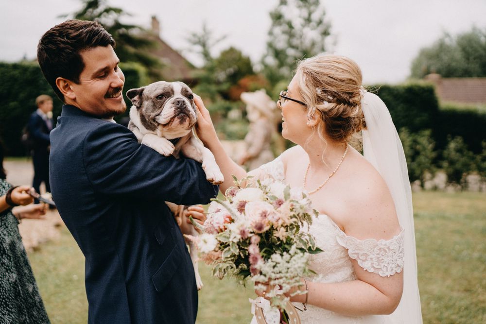 Joyful wedding celebration outdoors with a Boston Terrier dog being held up between the happy couple.