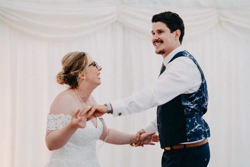 A couple dances joyfully together during a wedding reception in a white-draped venue.