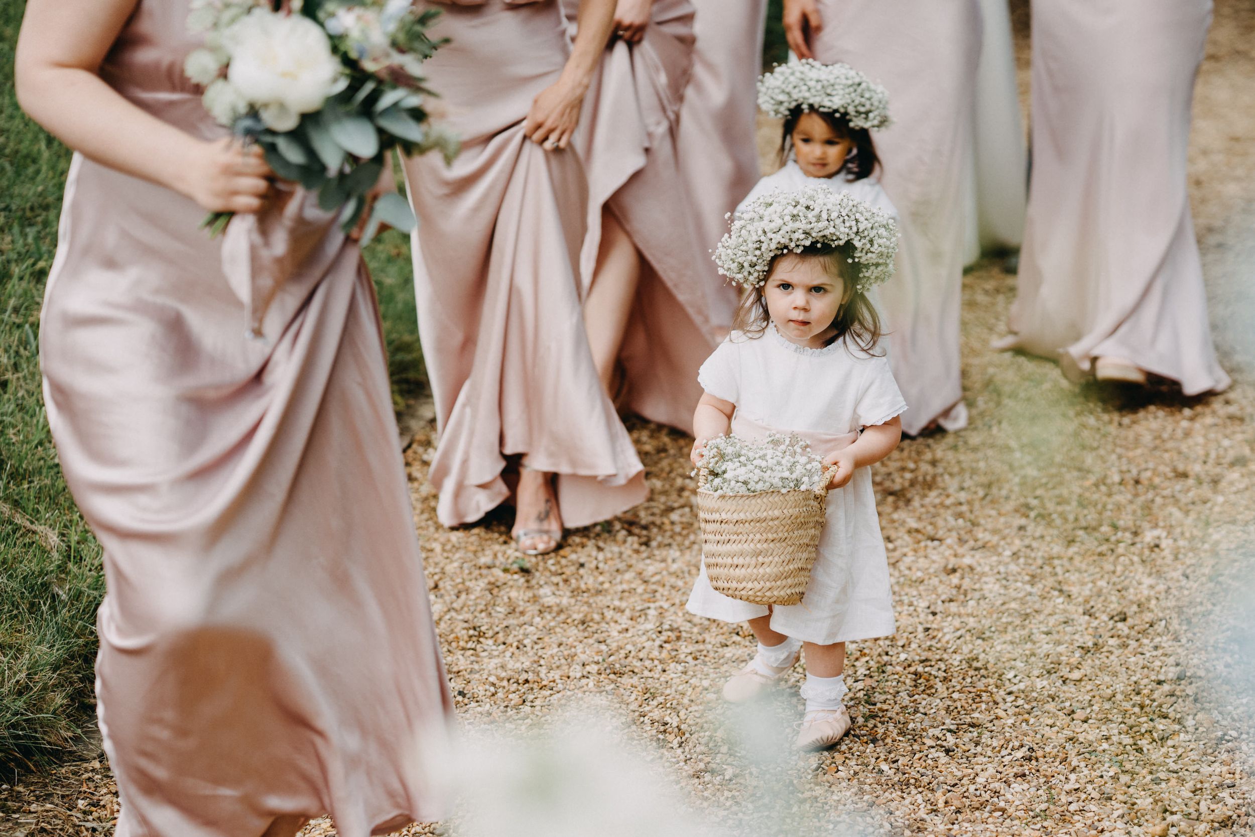 A group of people in blush pink dresses walking on a garden path for a wedding celebration.
