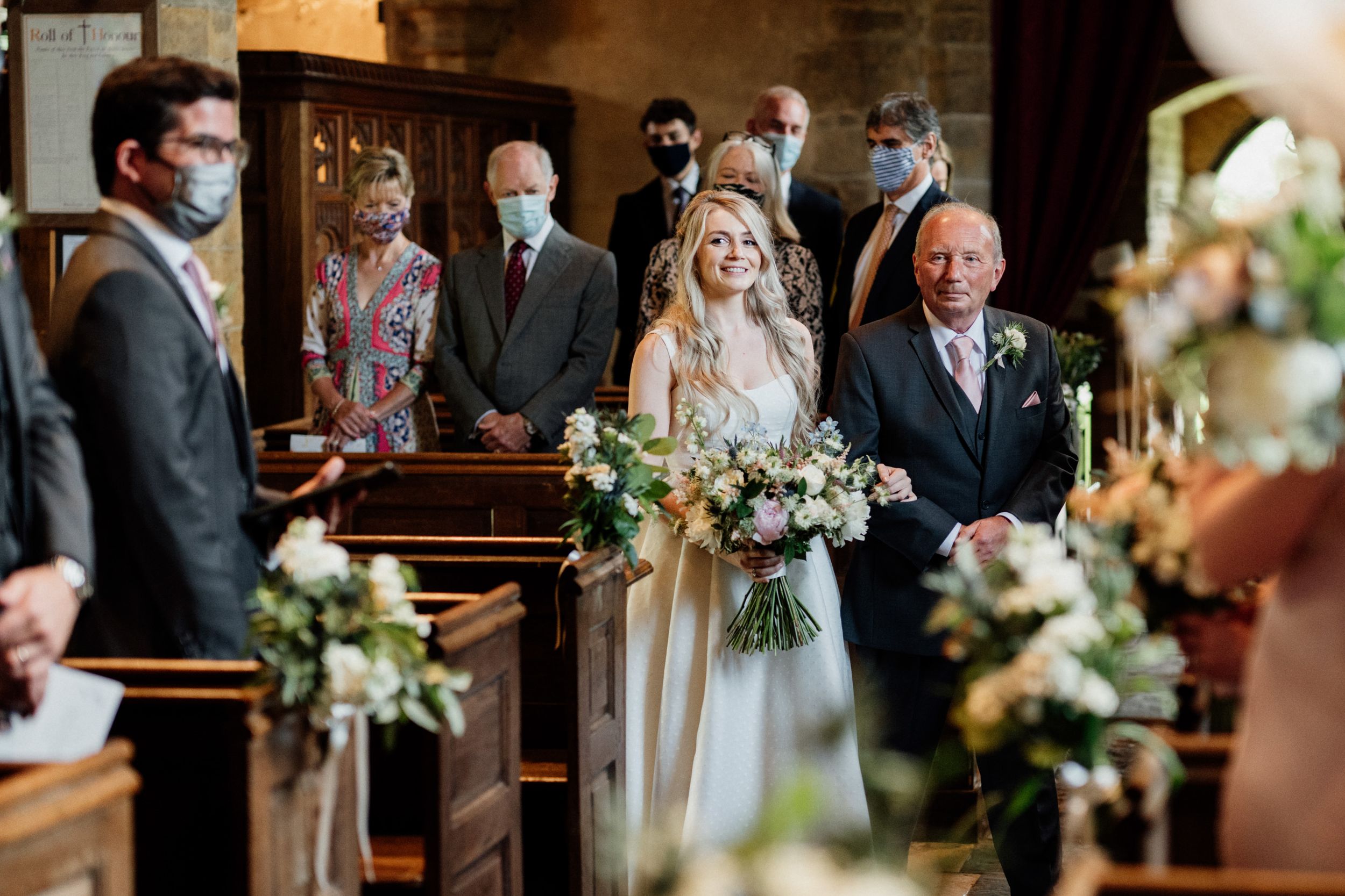 A wedding ceremony in a church with guests wearing protective face masks among floral decorations.