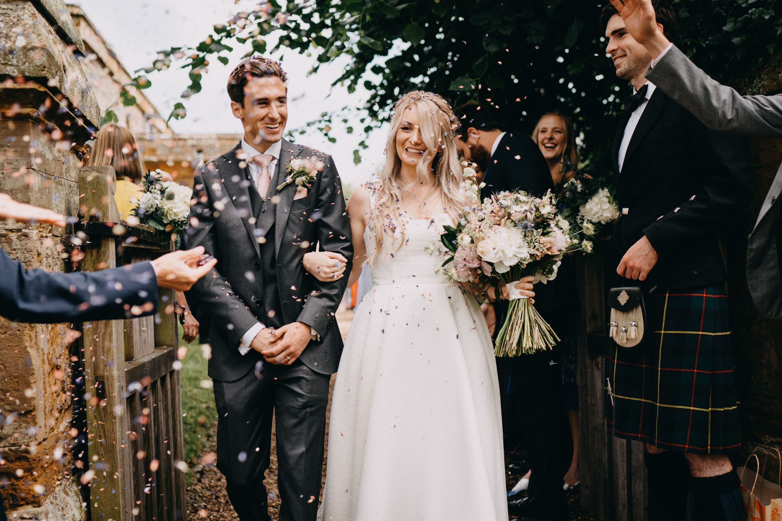 Newlyweds celebrate with confetti at a Scottish wedding ceremony with men wearing traditional kilts.