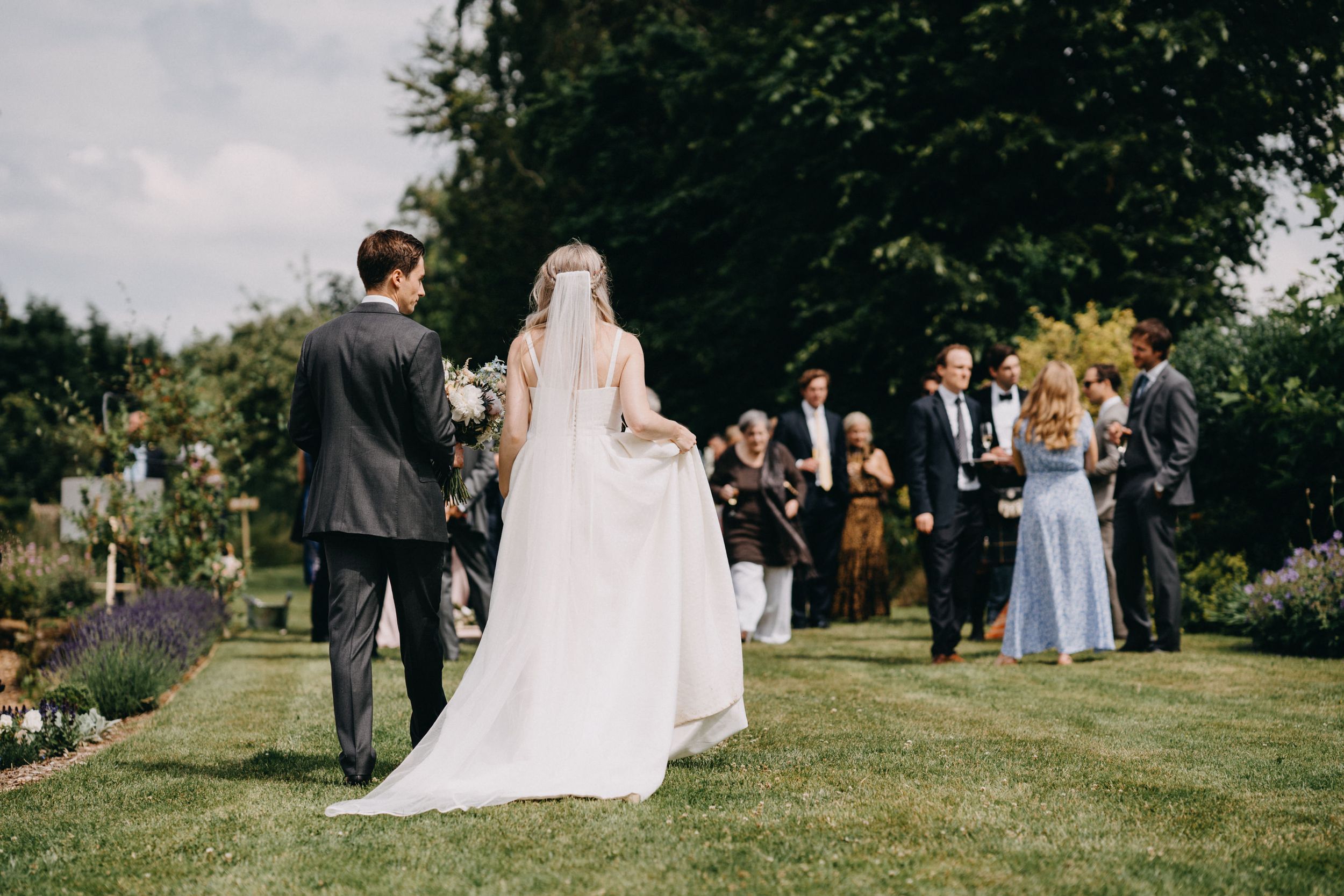 An outdoor garden wedding ceremony with guests gathered on a lush lawn while a couple stands together at the front.