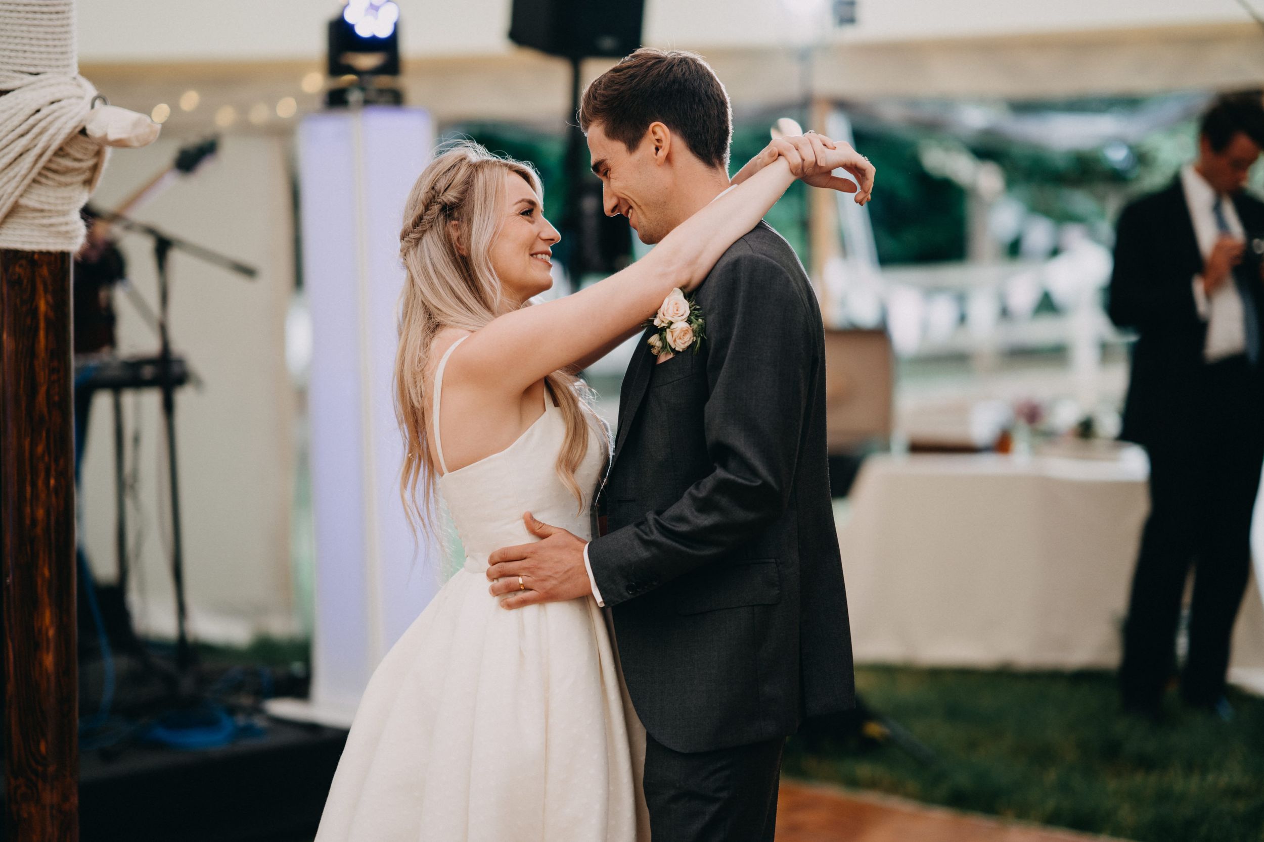 A couple shares their first dance together at an outdoor wedding reception with white tents visible.