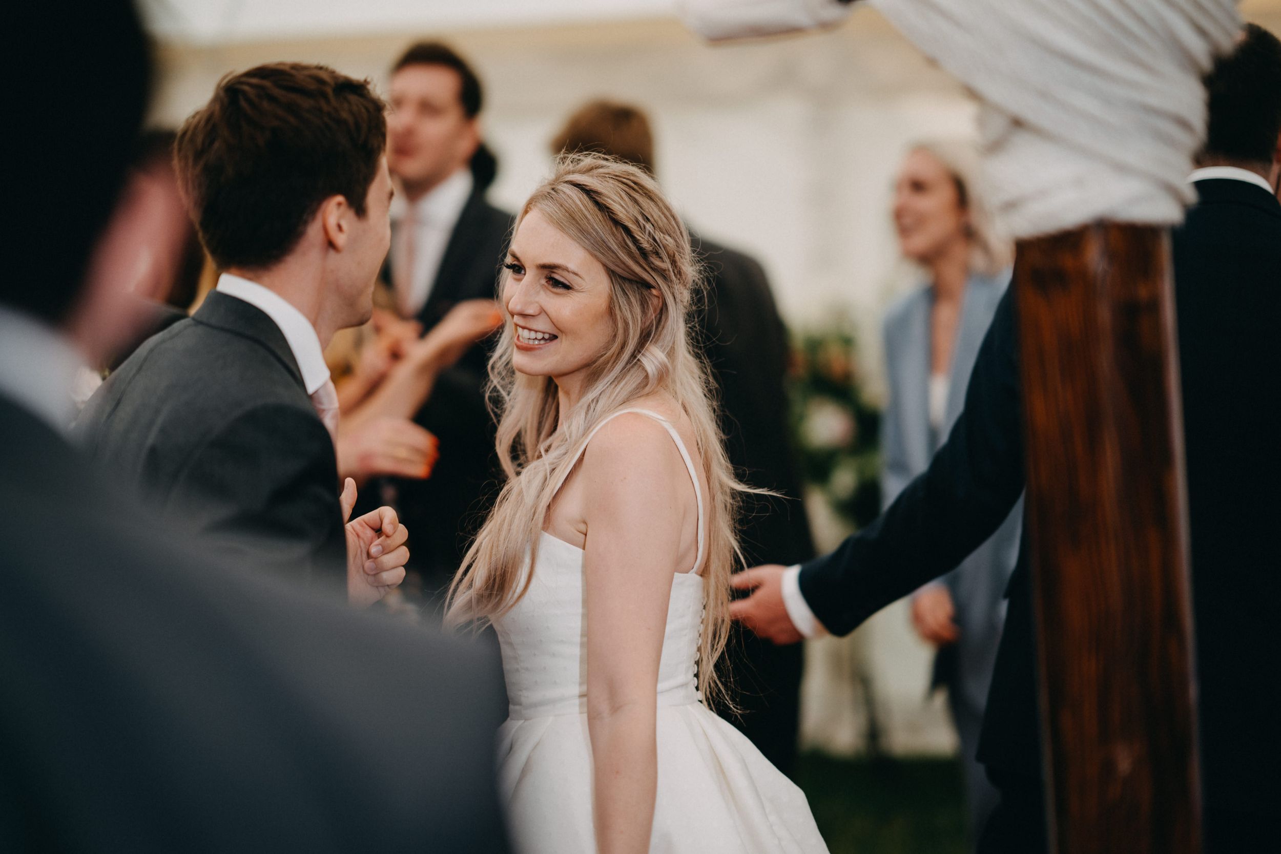 Wedding reception celebration with guests dancing and mingling under a white tent during golden hour.
