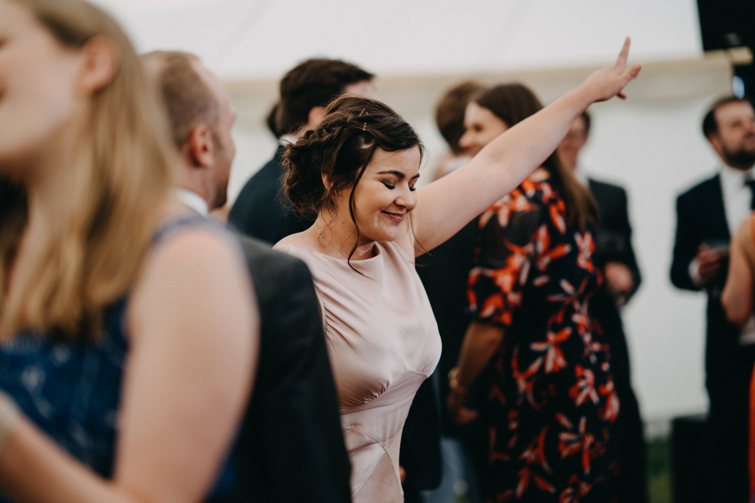 Joyful wedding guests dancing and celebrating with raised arms at a tented reception.