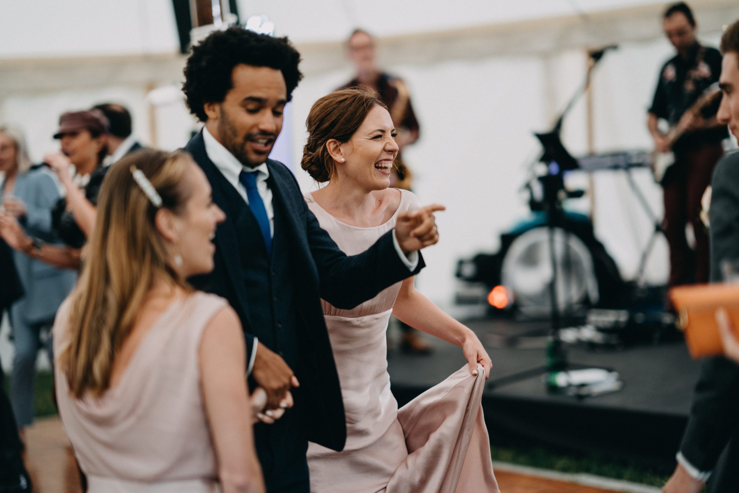 People dancing and celebrating at a wedding reception with a live band performing in the background.