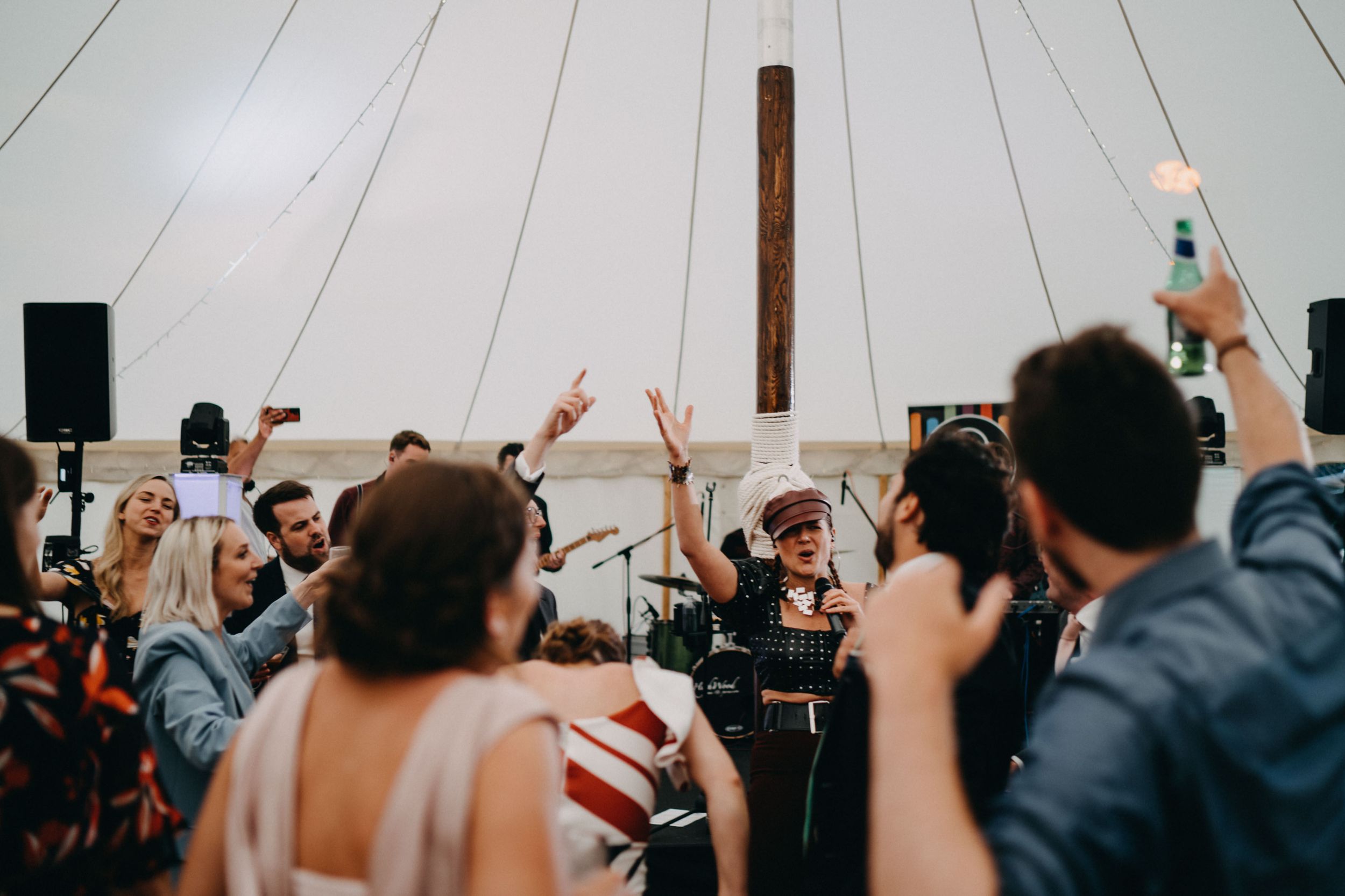 Energetic crowd dancing with raised hands at a lively wedding reception in a white tent venue.