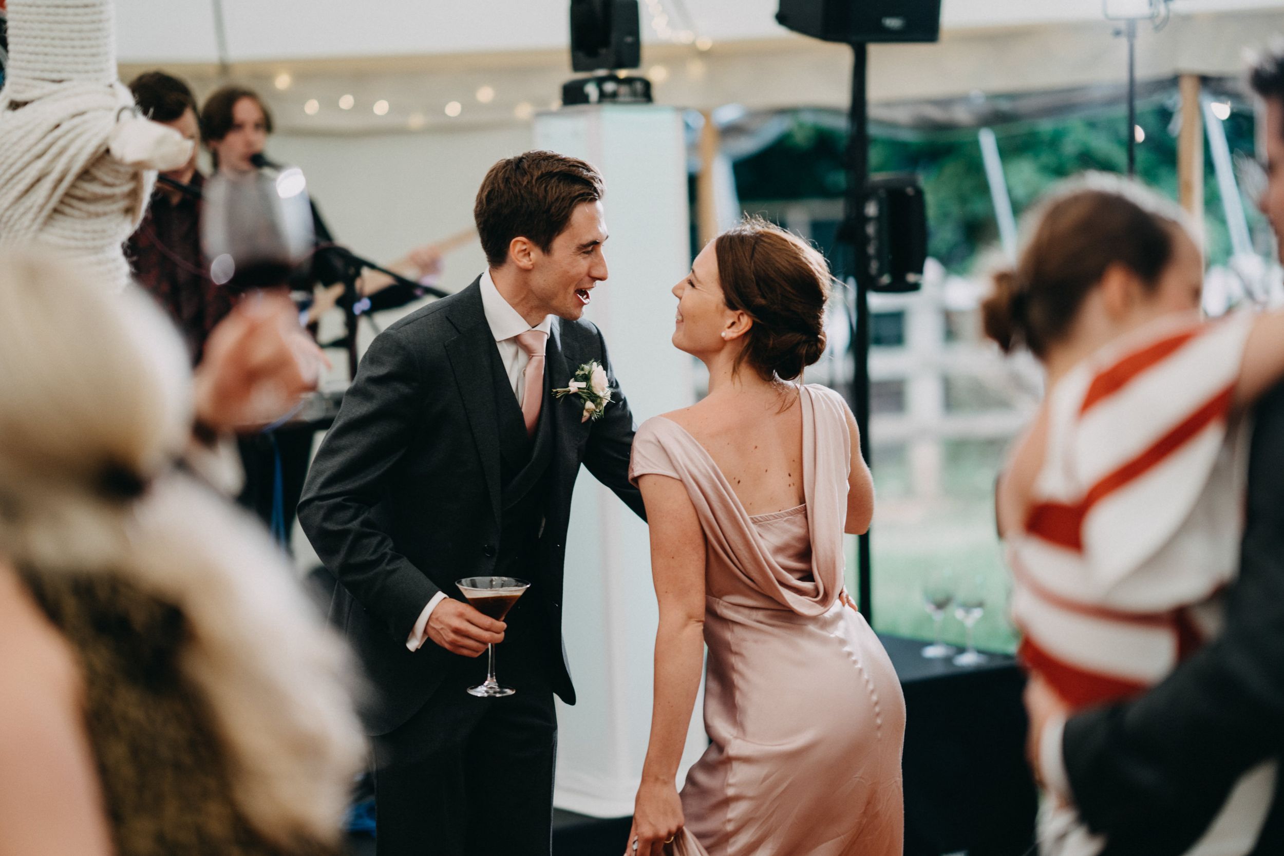 Wedding guests socializing and dancing in formal attire at an elegant tented reception party.