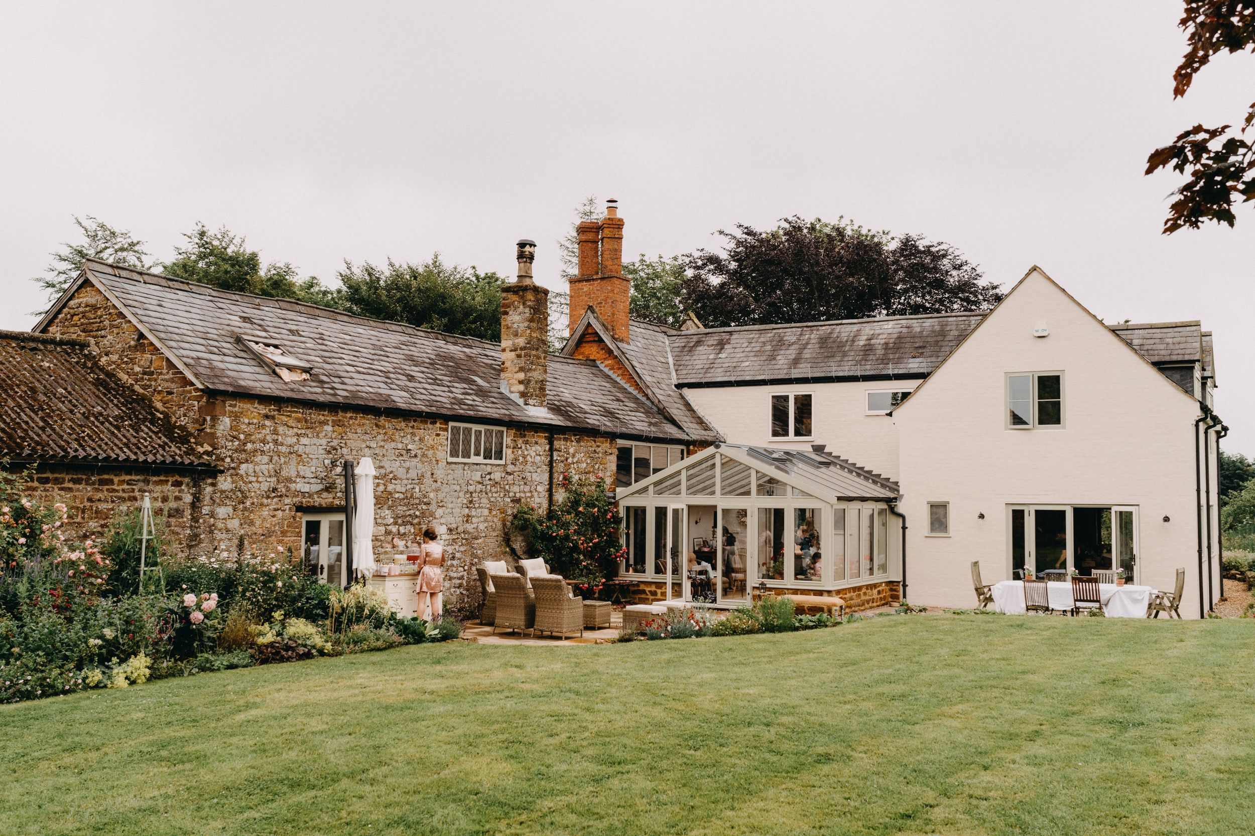A charming country house with stone walls, white extensions, and a conservatory overlooking a well-maintained lawn.