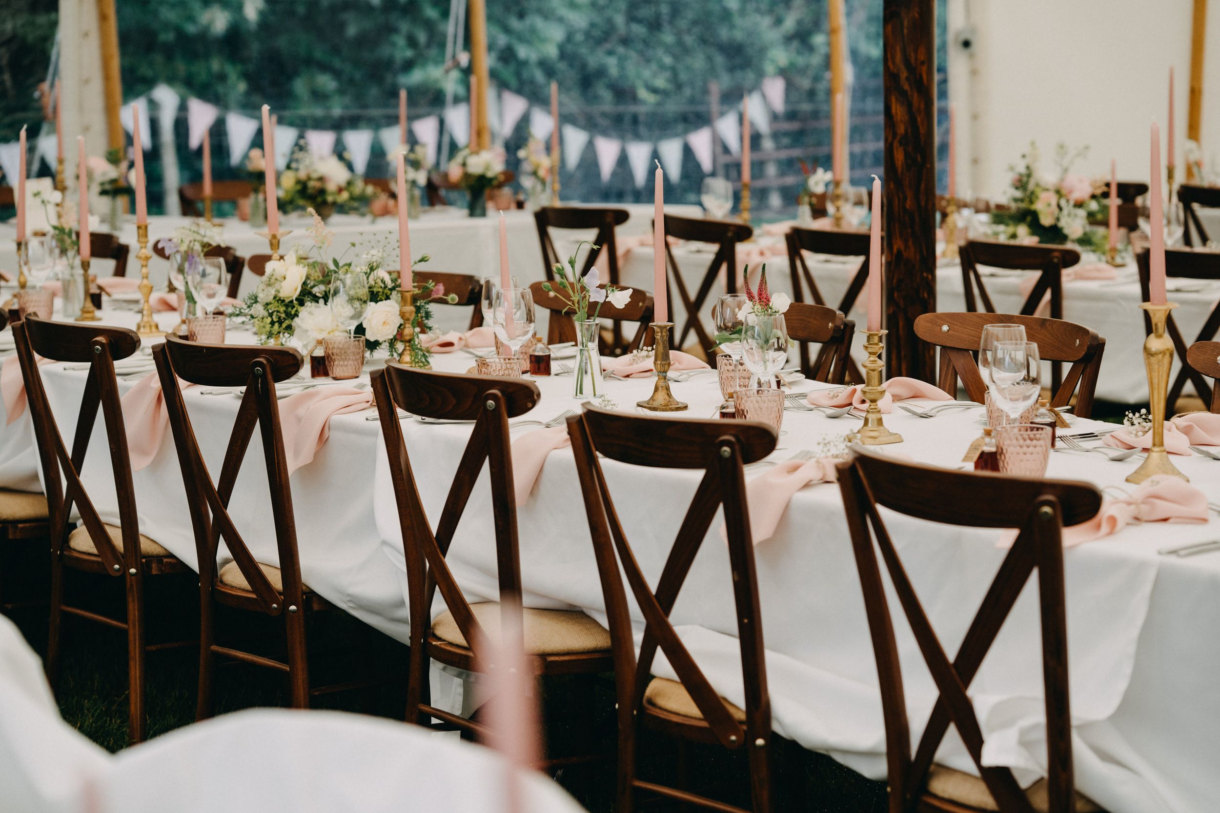 Elegant reception tables set with dark wooden cross-back chairs, white linens, and delicate floral centerpieces.