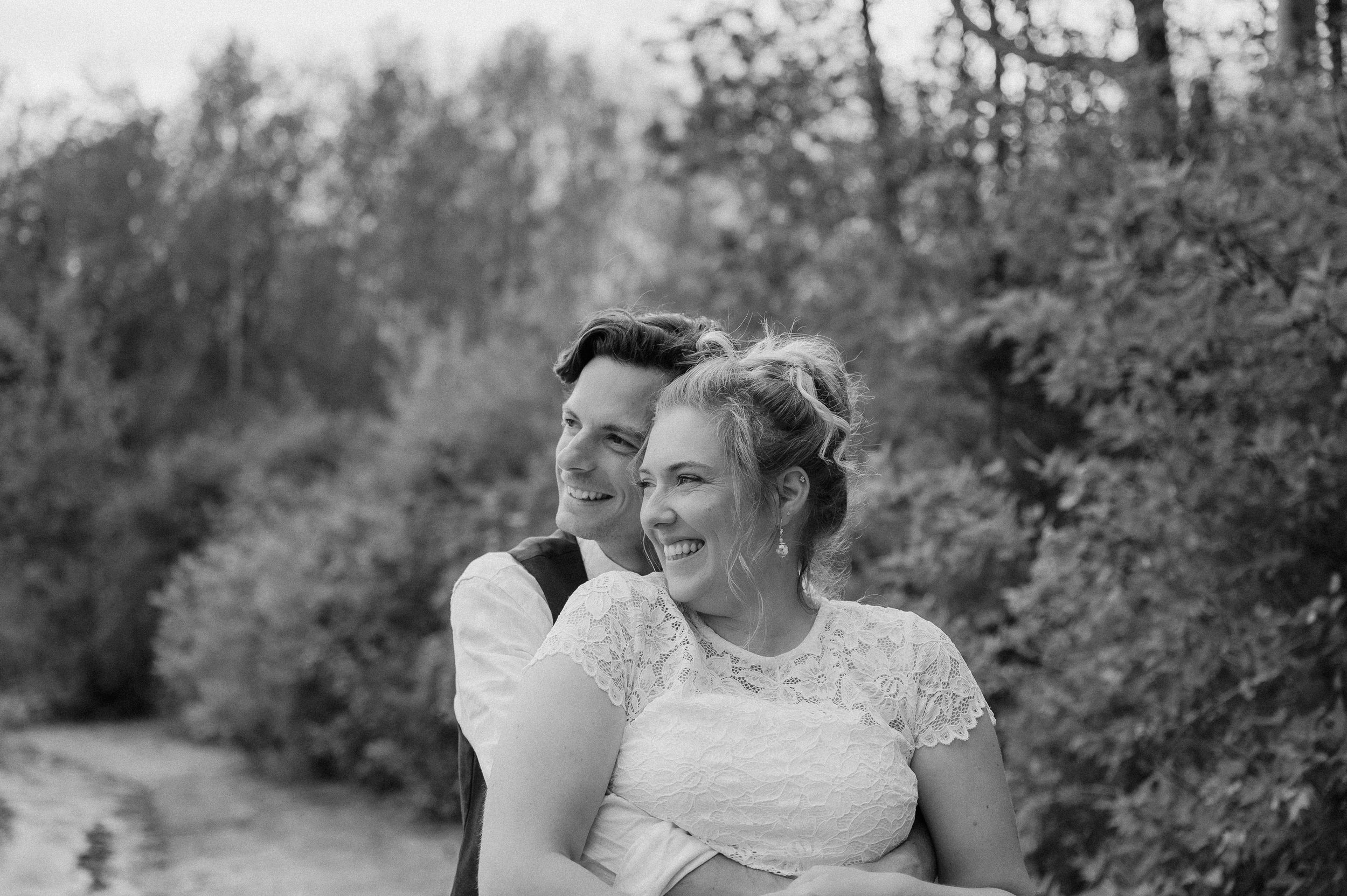 Black and white outdoor portrait of a joyful couple sharing a candid moment together on a wooded path.