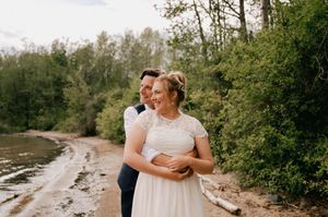 A couple embraces on a scenic shoreline surrounded by trees and natural beauty during a romantic photoshoot.