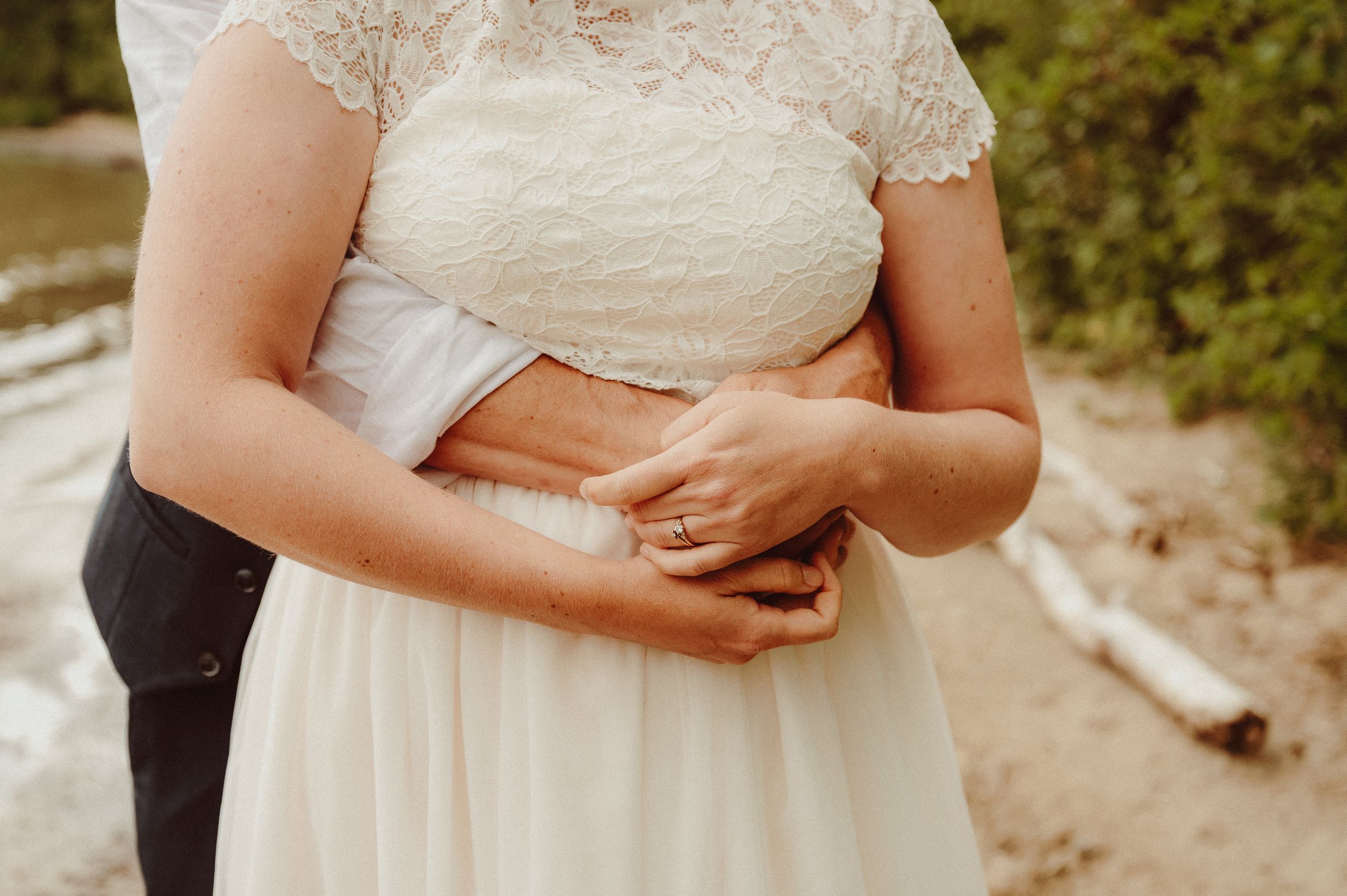 Two people embrace tenderly on a dirt path surrounded by greenery during a wedding photo session.