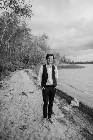 A series of connected black and white photos showing a person walking along a sandy beach shoreline on an overcast day.