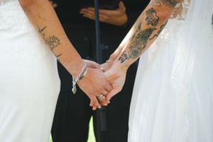 Close-up of tattooed hands clasped together during a wedding ceremony.