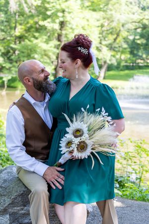 A couple in emerald green and brown attire share intimate moments together in a beautiful outdoor garden setting.