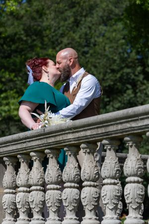 A romantic scene of a couple sharing a tender moment against an ornate stone balustrade in a garden setting.