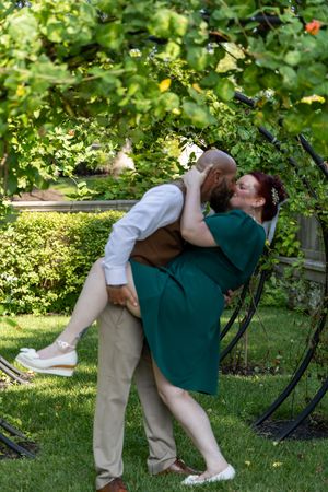 Two people share a playful dip in a lush green garden setting while dressed in casual attire.