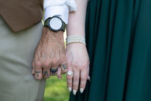 Close-up of hands with wedding rings and jewelry against a green background.