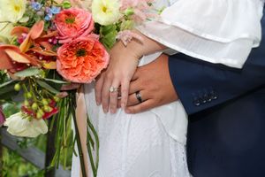 Elegant pink and orange floral bouquets are held in a wedding celebration against white dress fabric and dark suit details.