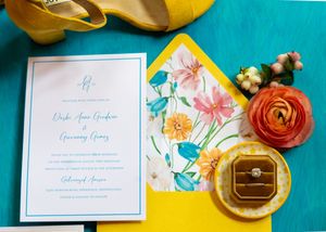Wedding stationery and floral decorations arranged on yellow and turquoise backgrounds in modern styled flat lay.
