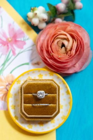 The pink rose blossoms sit framed behind sparkling diamond engagement rings resting on gold velvet jewelry boxes.