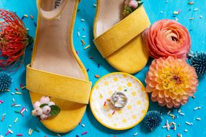 Yellow slide sandals and colorful dahlia flowers arranged on vibrant turquoise background with white sprinkles and donuts.