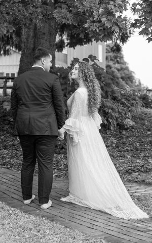 A couple in wedding attire sitting together on wooden steps surrounded by greenery in black and white photography.